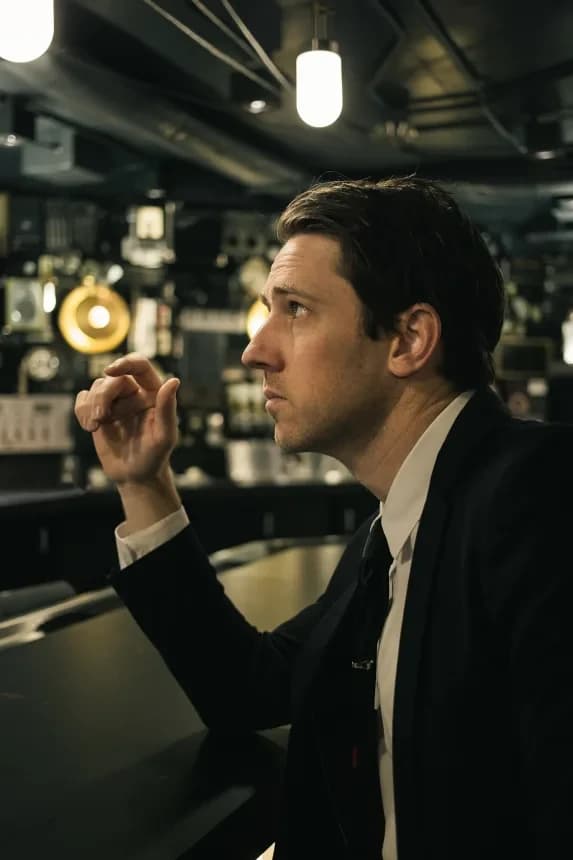 Chris Cron in profile, seated at a counter beneath pendant lights