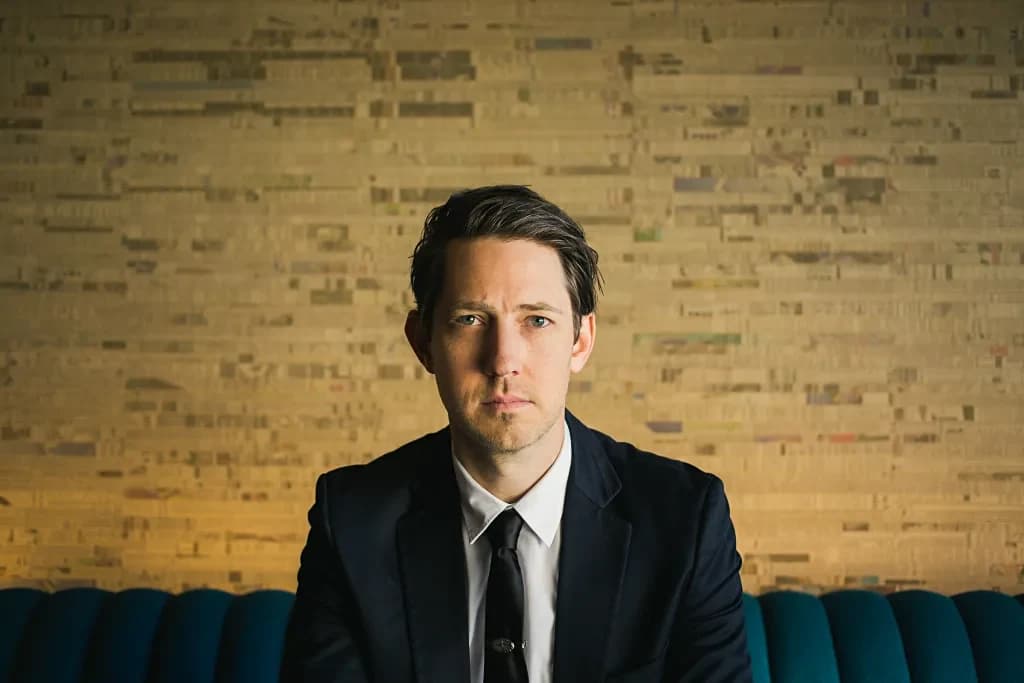 Chris Cron seated on a teal sofa in a dark suit and tie